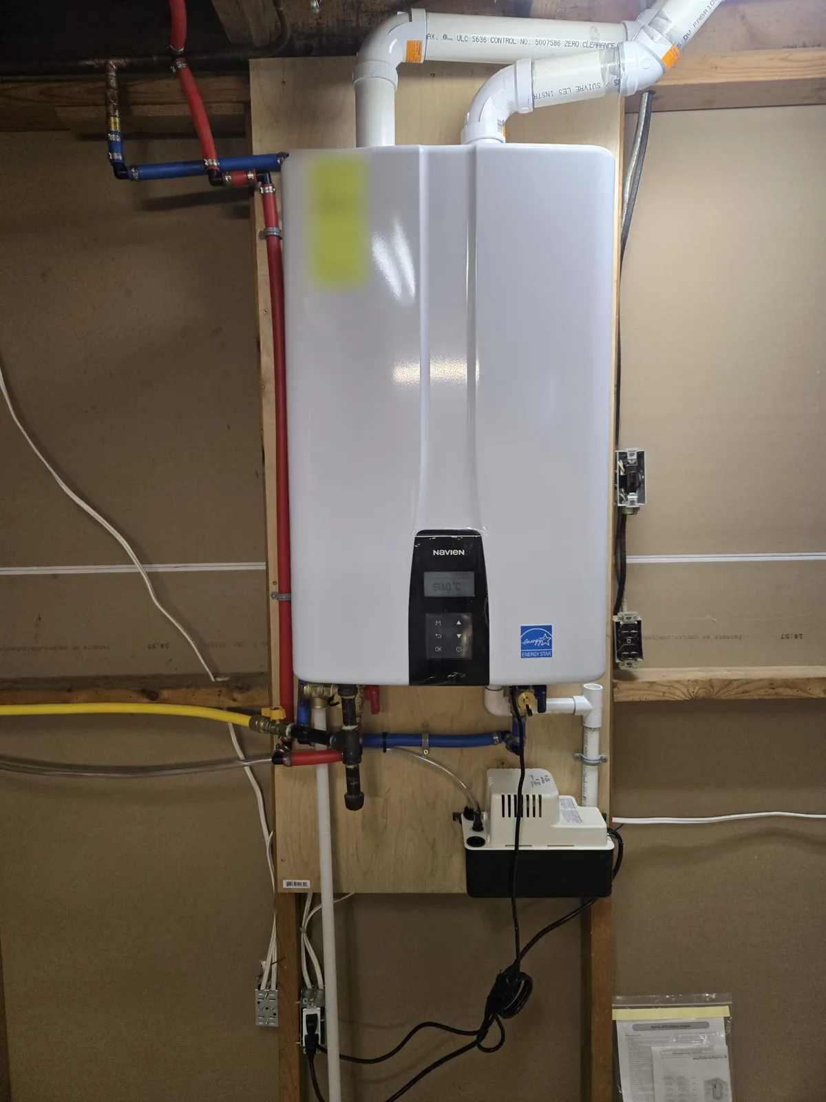 Navien tankless water heater close-up with PEX water lines, gas connection, PVC vent pipes and condensate pump