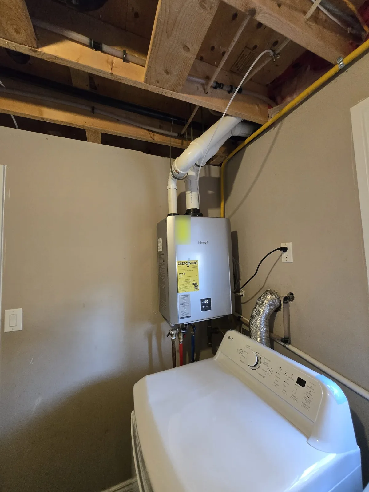 Rinnai tankless water heater installed in a laundry area with PVC venting, gas line and water connections